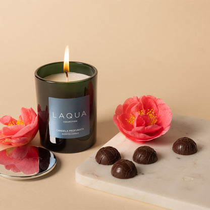 Candela profumata Vanille and Cigar accesa con fiori e cioccolatini su marmo
