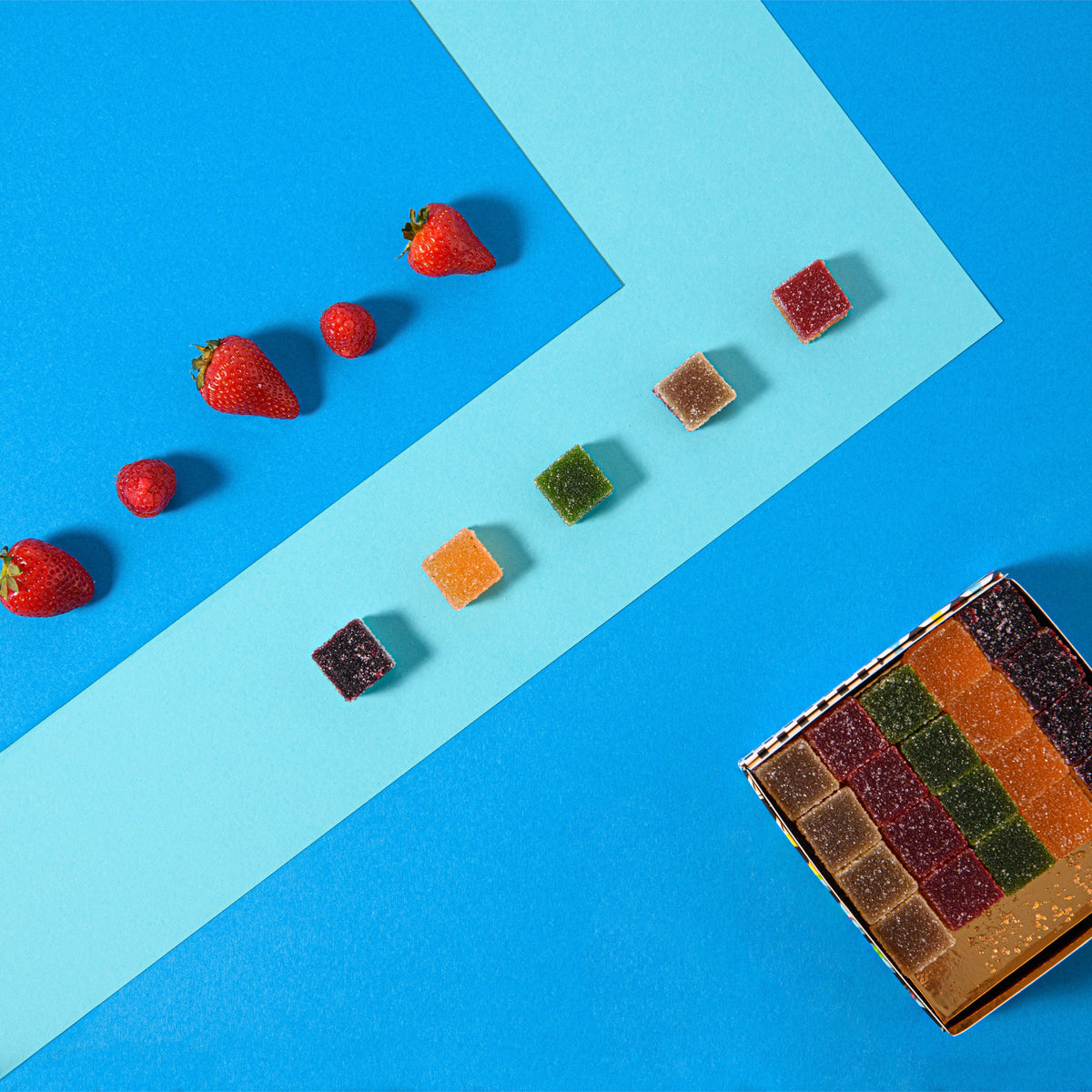 Caramelle gelée alla frutta colorate e fragole su sfondo azzurro, con scatola aperta