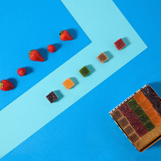 Caramelle gelée alla frutta colorate e fragole su sfondo azzurro, con scatola aperta